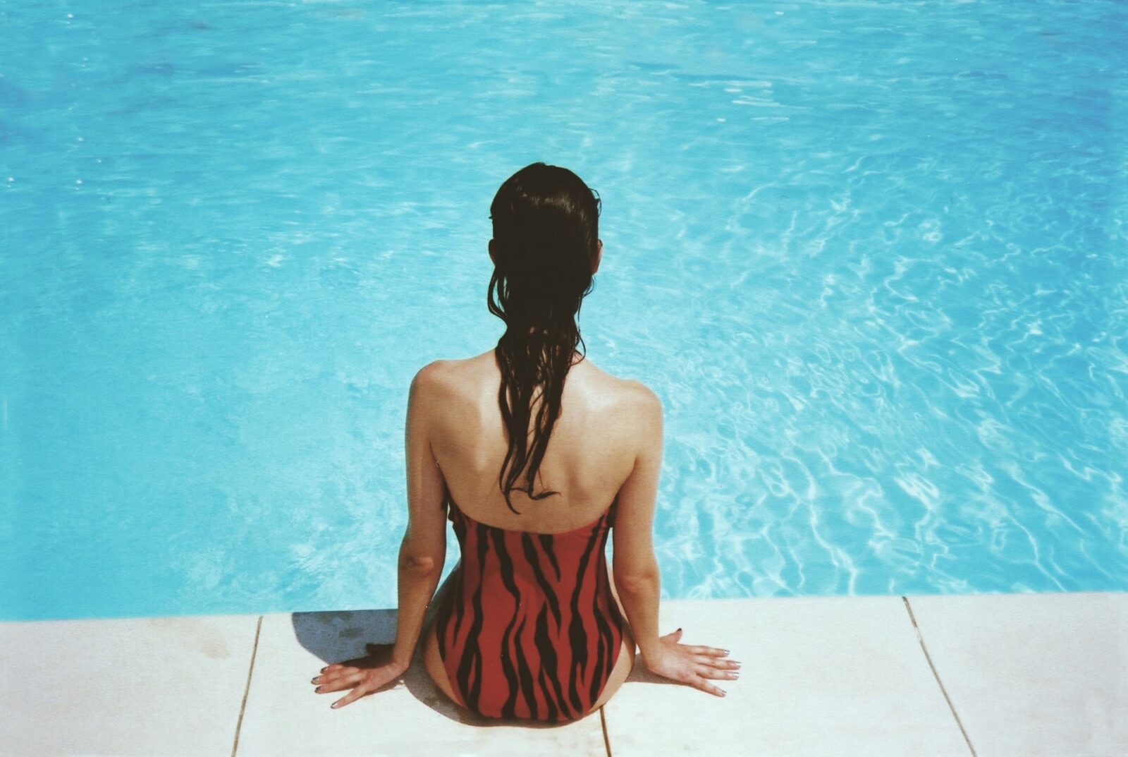 woman sitting beside swimming pool while dangling her feet in the water