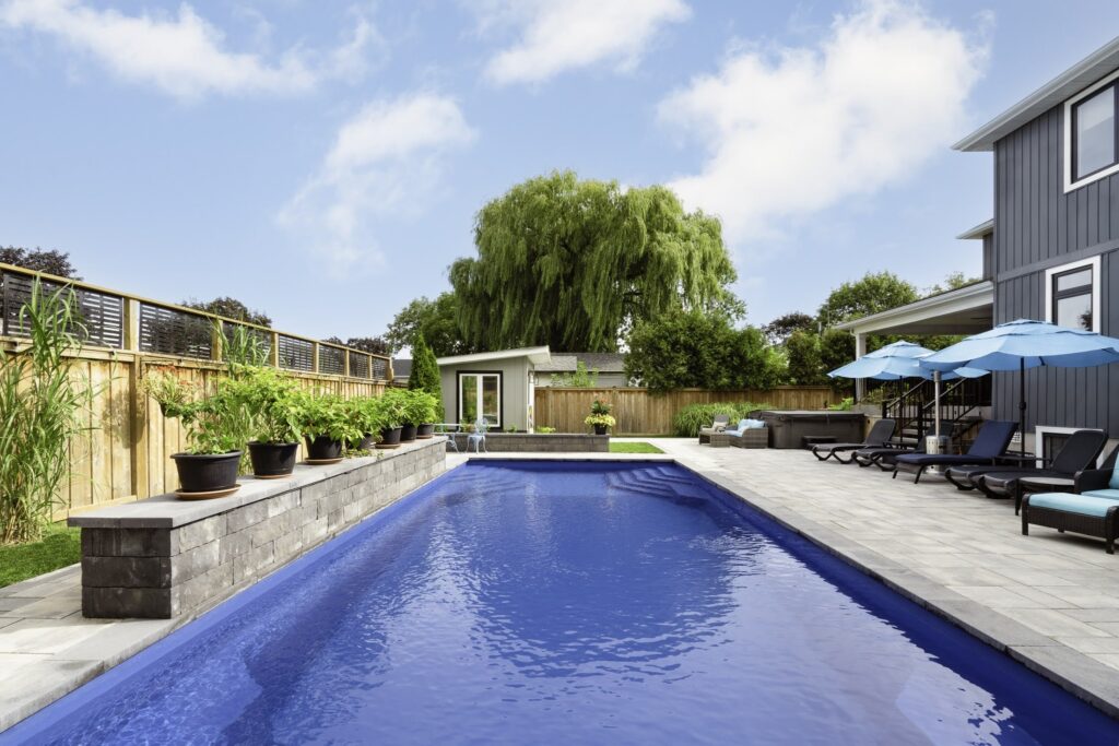 Elmwood Cres Ontario, rectangular fiberglass swimming pool surrounded by smooth pavers and lush plants 